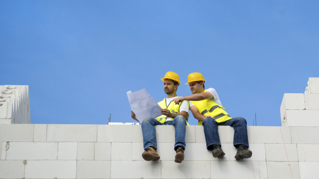 Dois homens da construção civil sentados em cima de blocos de concreto